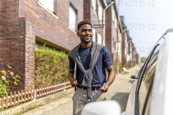 African young businessman going to work by car opening it by remote control while carrying laptop in the street