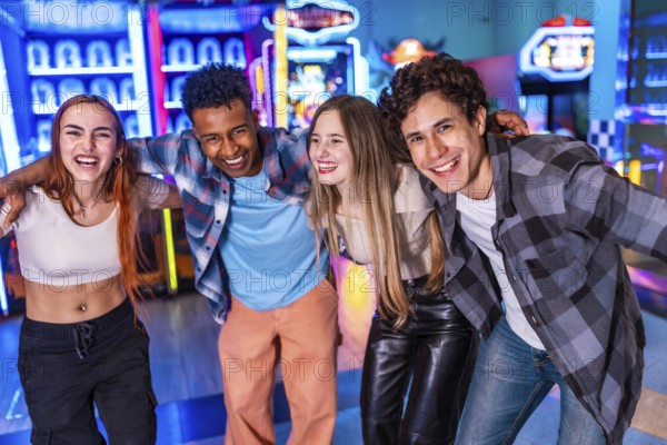 Four young cheerful multi ethnic friends are hugging each other, smiling and having fun together at the amusement arcade