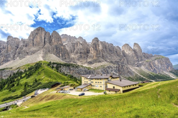 Green meadows and a mountain hotel are surrounded by the breathtaking peaks of the dolomites on a sunny summer day