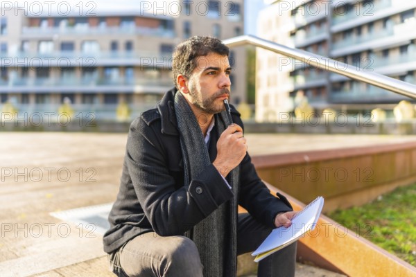 Pensive casual businessman writing notes sitting on urban stairs in autumn