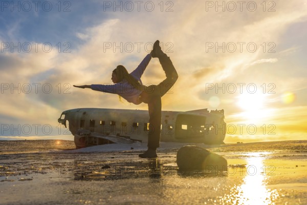 Woman on the Solheimasandur plane in Iceland performing a Natarajasana yoga pose to open the hip and heart
