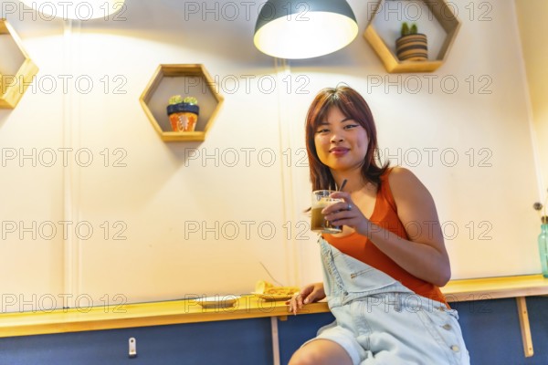 Low angle view portrait of an asian cool young woman smiling at camera sitting drinking coffee in a cafeteria