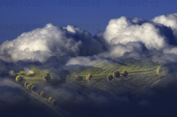 Hilly landscape with trees enveloped by dramatic clouds and fog in a surreal atmosphere, Wenden, North Rhine-Westphalia, Germany, Europe