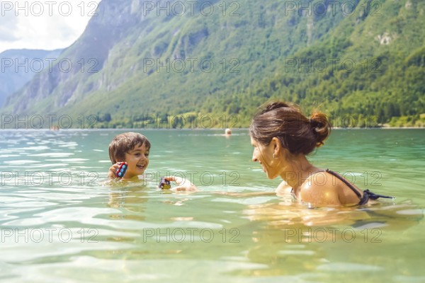 Mother and son enjoying summer fun, playing with toys while swimming in the refreshing waters of lake bohinj, surrounded by the julian alps