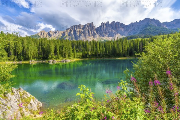 Stunning view of the emerald green water of lake carezza with the latemar mountain range in the background, dolomites, south tyrol, italy