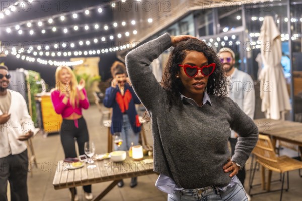 Sensual latin woman with sunglasses and casual winter clothes dancing next to friends at night party in a roof bar terrace