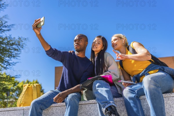 African man taking selfie with multi-ethnic friends in the university campus sitting outside on a wall