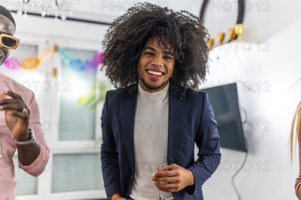 Latin cheerful man with curly hair smiling at camera during home party with friends