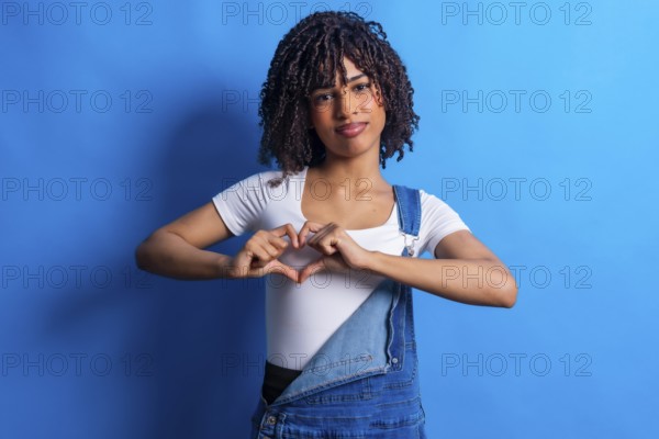 Studio portrait featuring a young woman forming a heart shape with her hands, radiating love and positivity against a vibrant blue background
