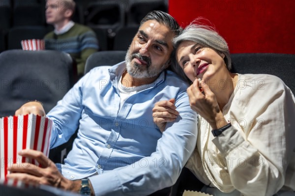 Senior couple enjoying a cozy movie night at the cinema, savoring popcorn while sharing a heartfelt moment filled with joy and affection