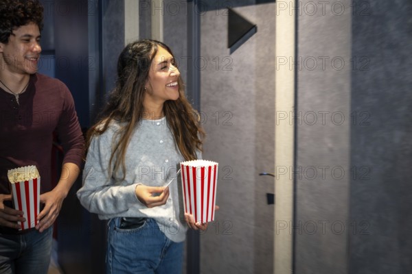 Happy couple walking into a movie theater, holding popcorn buckets and tickets, excited for the show