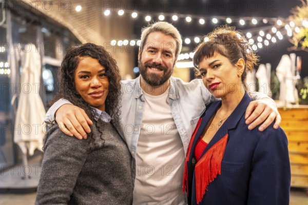 Portrait of three multi-ethnic friends embracing and smiling at camera at night party