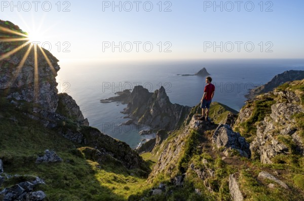 Mountaineer on the summit of Måtind or Måtinden, view of picturesque coastal landscape with sun star, rocky coast and sea, Andøya Island, Vesterålen, Nordland, Norway, Europe