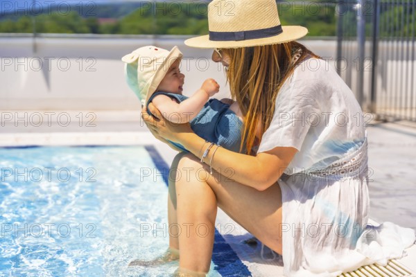 Side view of a mother and cute baby with sun hat in the swimming pool