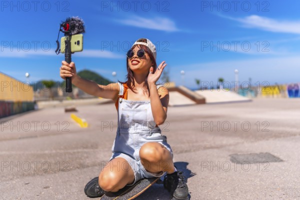 Asian young woman are doing livestreaming joyfully in skateboard urban park waving at the camera while recording
