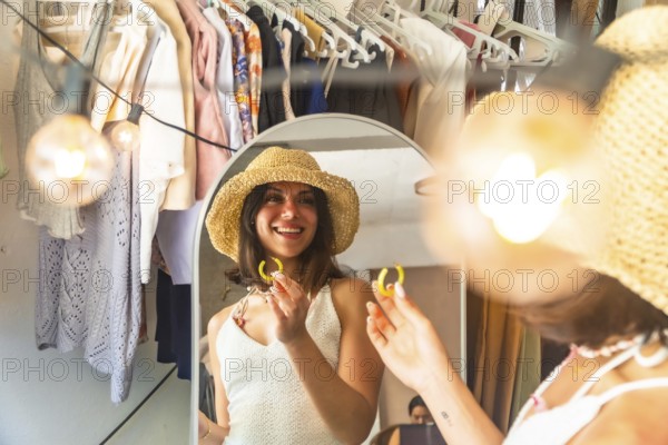 Young woman wearing straw hat trying on yellow earrings, getting ready in front of a mirror in her hotel room or bungalow in siargao island, philippines