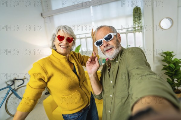 Senior couple with fashionable sunglasses taking selfie while having fun at home