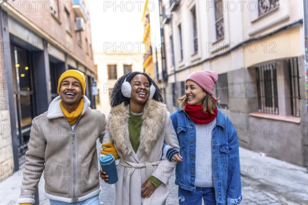 Three happy friends are walking arm in arm down a city street, laughing and enjoying each other's company during the winter season
