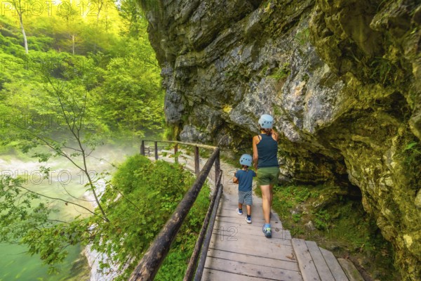 Tourists wearing helmets are enjoying a hike through the scenic vintgar gorge near bled, slovenia, walking along a wooden footbridge over a clear river