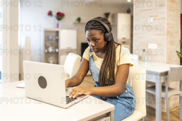 Young student concentrating on her laptop, wearing headphones, diligently working on school assignments in a comfortable home setting