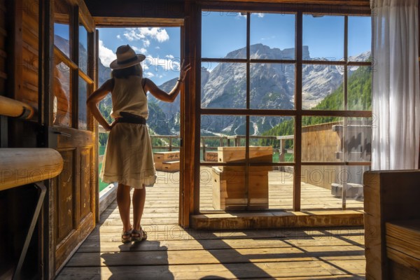 Woman enjoying breathtaking views of lake braies and surrounding mountains from a traditional wooden cabin in the italian dolomites