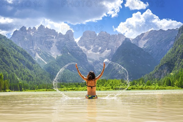Young woman enjoying a refreshing swim in the scenic lago di landro, dolomites, italy, splashing water with majestic mountains in the background