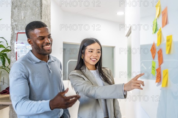 Smiling businesspeople analyzing project plan using colorful sticky notes on whiteboard in modern coworking office