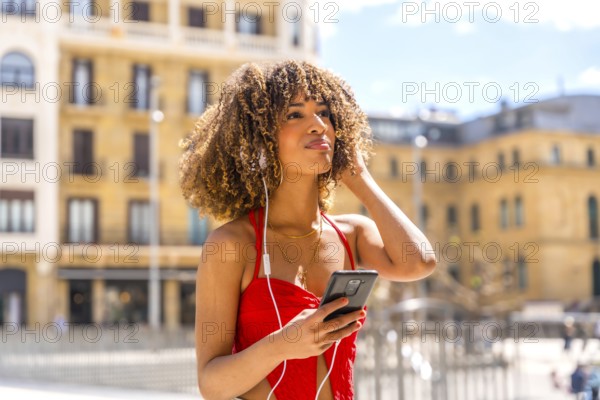 Hispanic woman with curly hair listening to music using mobile at the city