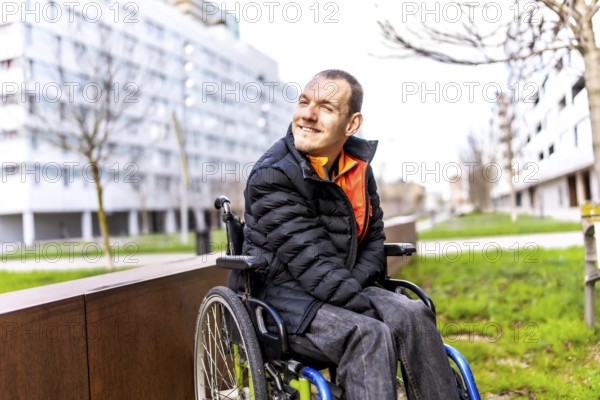 Young man using wheelchair smiling while enjoying a day out in an urban park, promoting inclusion and accessibility