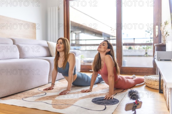 Two young women practicing yoga at home, following an online class on their smartphone during lockdown