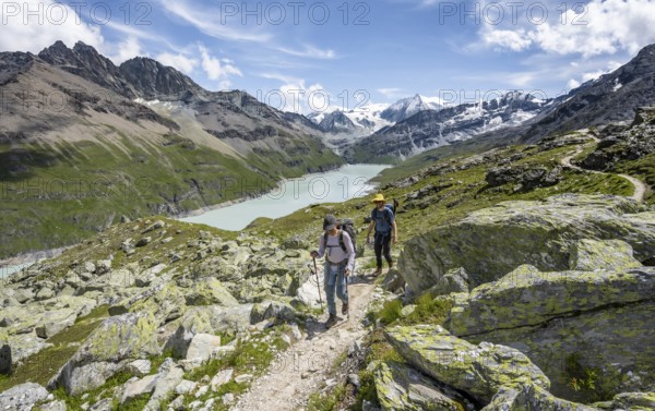 Two mountaineers on a hiking trail, view of a blue mountain lake, Lac des Dix reservoir, mountain peak Mont Blanc de Cheilon in the background, Hérménence, Valais Alps, Valais, Switzerland, Europe