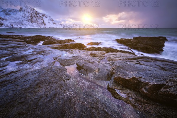 Beach of Norwegian sea on rocky coast in fjord on sunset in winter. Vareid beach, Lofoten islands, Norway, Europe