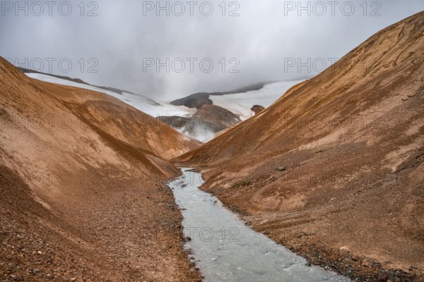 Steaming stream between colourful rhyolite mountains and snowfields, Hveradalir geothermal area, Kerlingarfjöll, Icelandic Highlands, Iceland, Europe