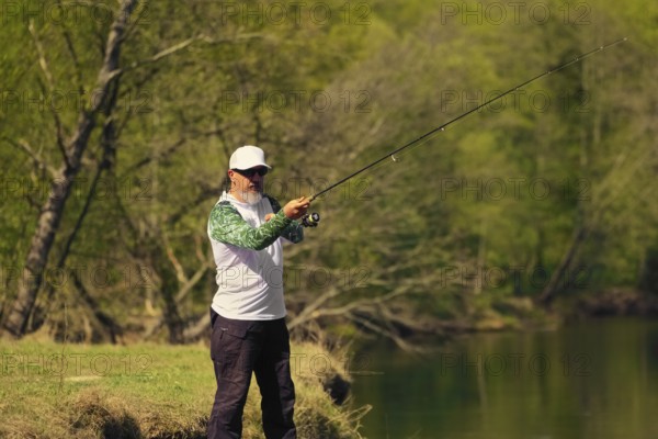 Man fish with spinning on river bank, casting lure. Outdoor weekend activity. Photo with shallow depth of field taken at wide open aperture