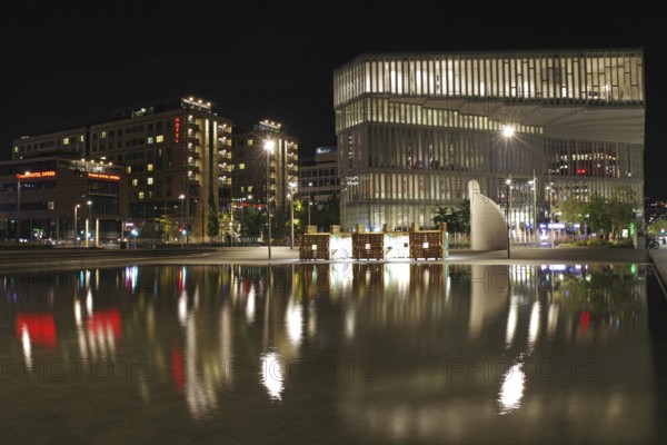 Modern buildings with luminous facades are reflected in a calm body of water at night, hotels, modern architecture, Oslo, Norway, Europe