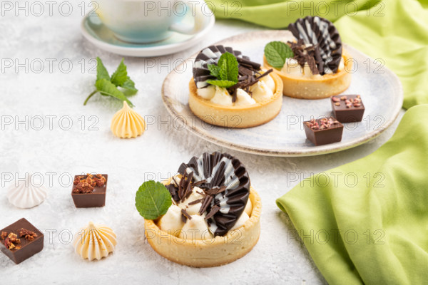 Sweet tartlets with chocolate and cheese cream with cup of coffee on a gray concrete background and green textile. Side view, close up