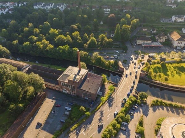 Aerial view of an industrial building cloth and ceiling factory with chimney next to a road with cars, near a river and surrounded by trees, Calw, Black Forest, Germany, Europe