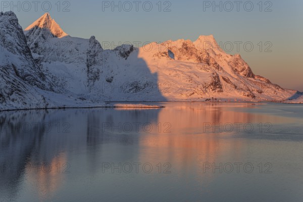 Snow-covered mountains reflected in the fjord at sunrise, winter, Reine, Moskenesoya, Lofoten, Norway, Europe