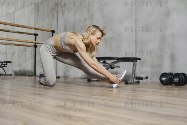 Fitness woman bends forward stretching the muscles of her back and legs in gym