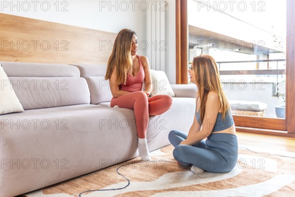 Two women enjoying an online class, practicing yoga and meditation in a cozy living room setting with natural light and modern decor