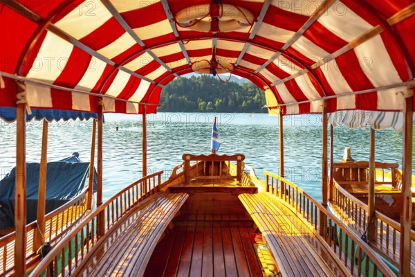 Wooden tourist boat with red and white canopy sailing on lake bled in slovenia, offering scenic view of bled island