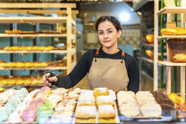 Latin young saleswoman next to a counter full of colorful pastries to sell in a bakery