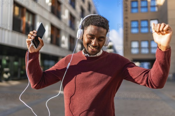Happy african man listening to music with mobile and headphones dancing in the city street