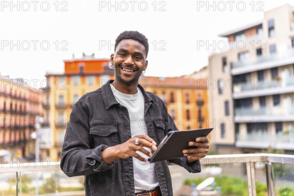 African young man smiling at camera while using digital tablet in the city