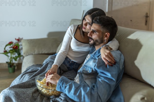 Romantic couple sharing a bowl of popcorn while watching a movie on television in their living room at night