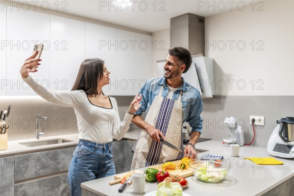 Young couple taking selfie with smartphone while preparing a healthy vegetarian salad in a modern kitchen