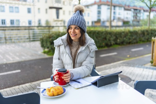 Beauty woman wearing warm clothes and woolly hat warming hands with hot coffee in a sidewalk cafeteria