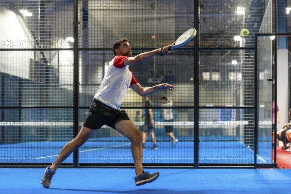 Full length photo of a mature sportive man trying to reach the ball while playing paddle tennis in an indoor court
