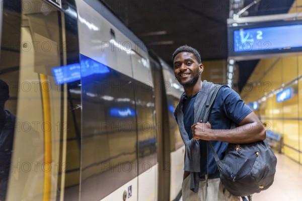 African young businessman waiting for the metro at night standing on the platform and smiling at camera