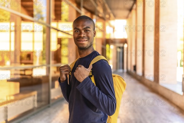 Happy african american student standing with rucksack smiling at camera at the corridor of the university